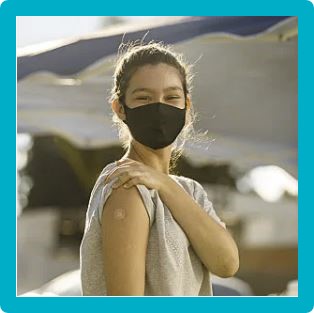 Photo of a woman with a mask on her face, pulling up the sleeve on her arm, showing her band aid where she got the vaccine