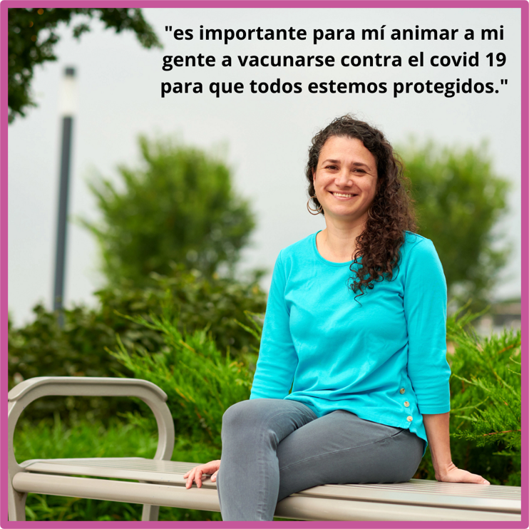 Photo of woman sitting outside on a bench, smiling, plants behind her